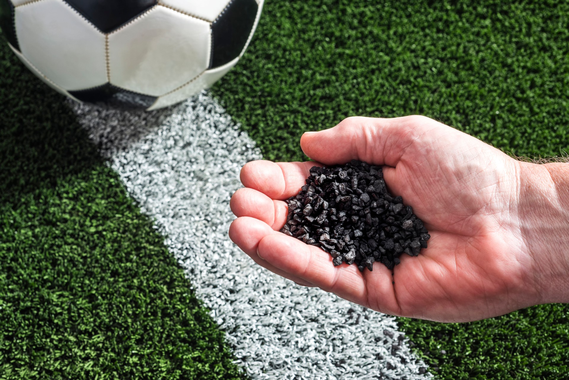 Hand holding crumb rubber over an artificial turf sports field